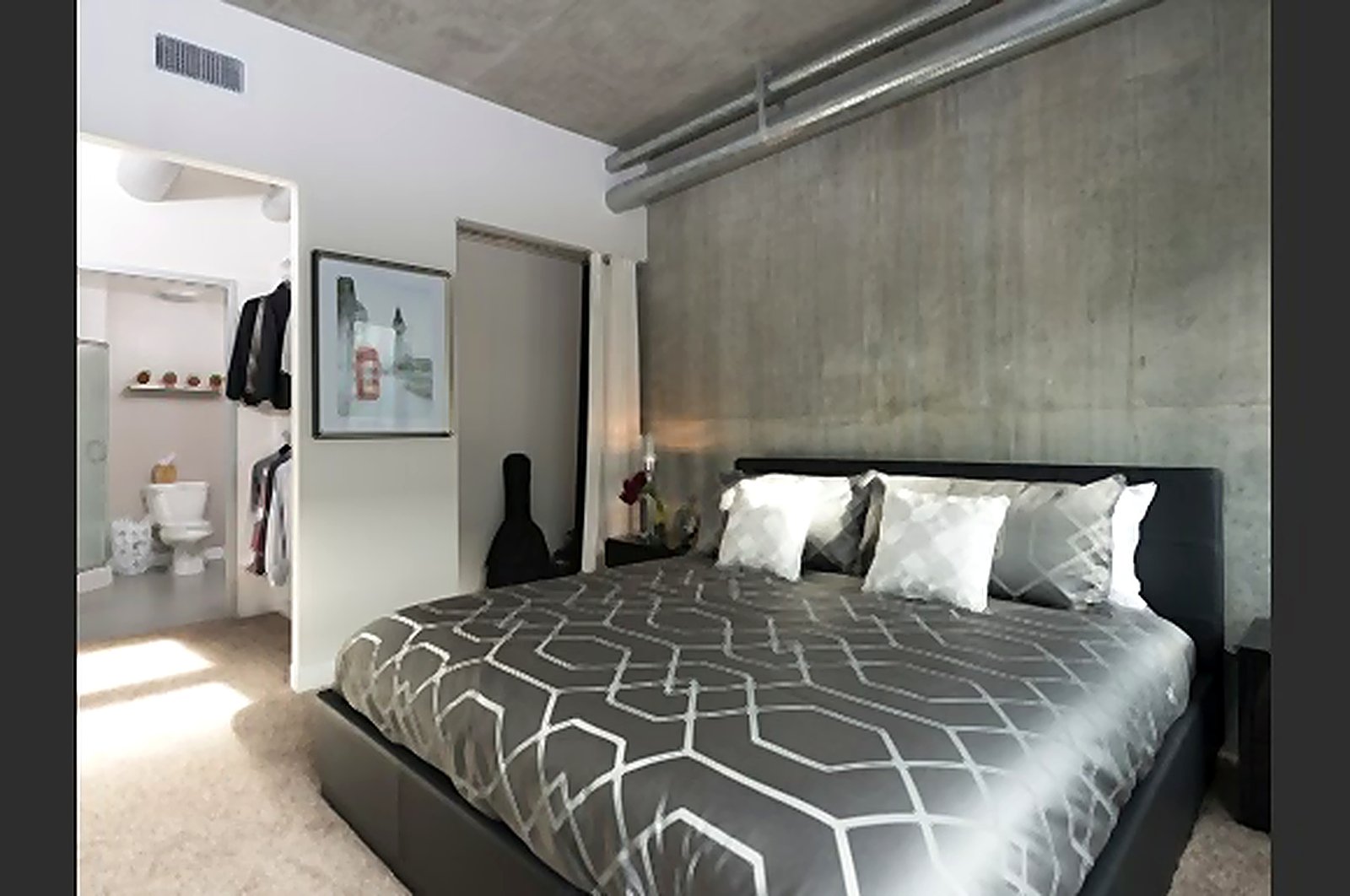 Downtown LA furnished apartment bedroom with geometric bedding and exposed concrete accent wall